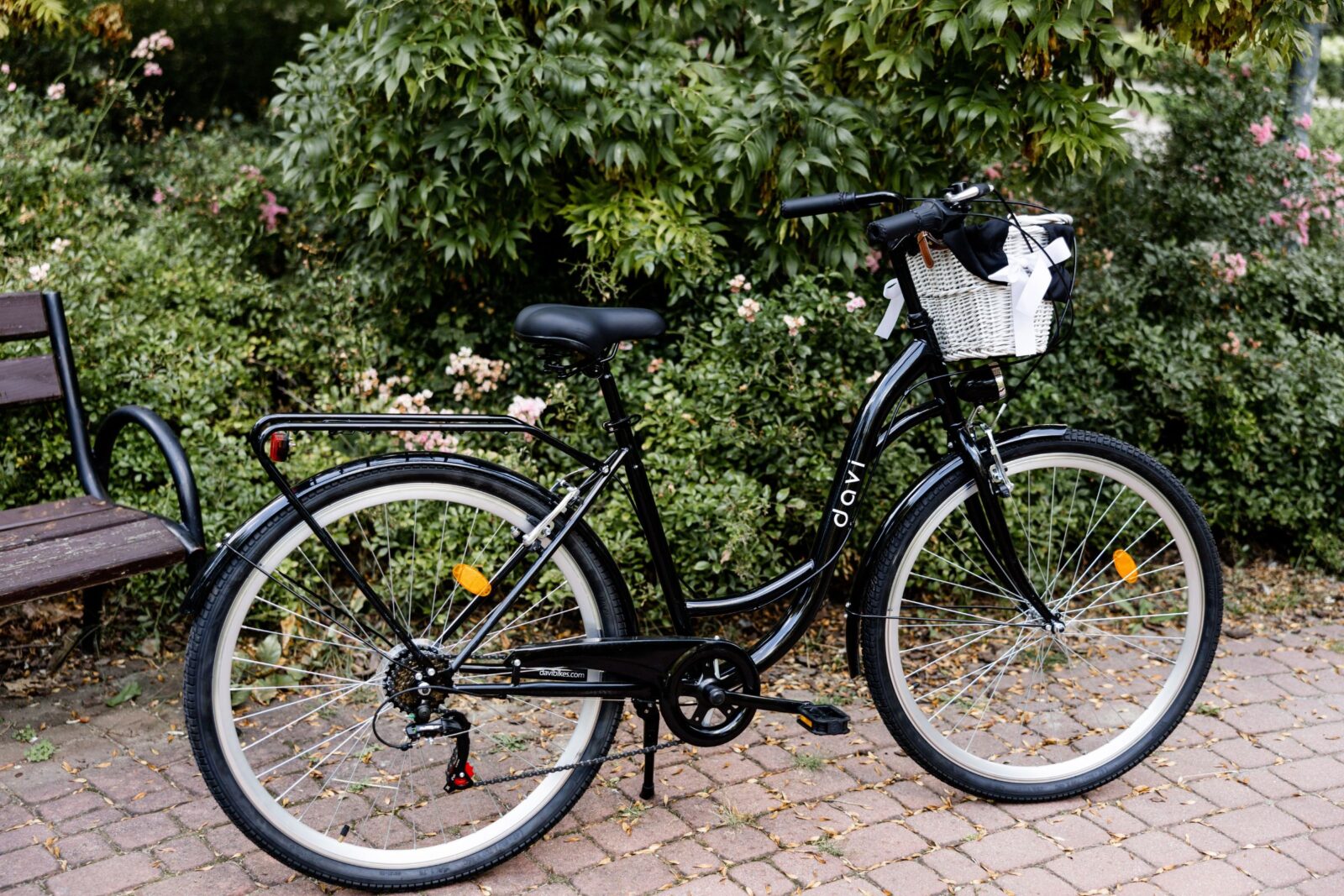 Fekete bicikli virágos parkban pad mellett.