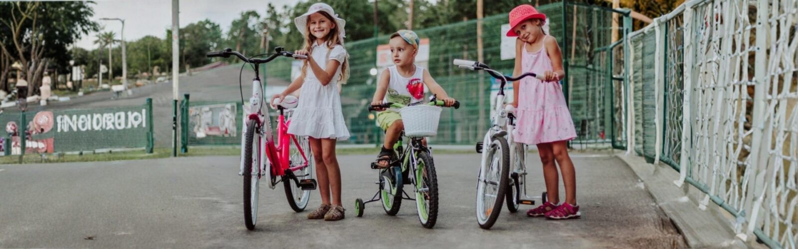 Gyerekek bicikliznek parkban nyáron, színes ruhákban.