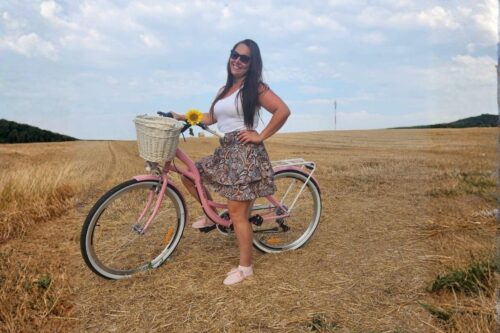 Mosolygós nő biciklizik napraforgóval a mezőn.